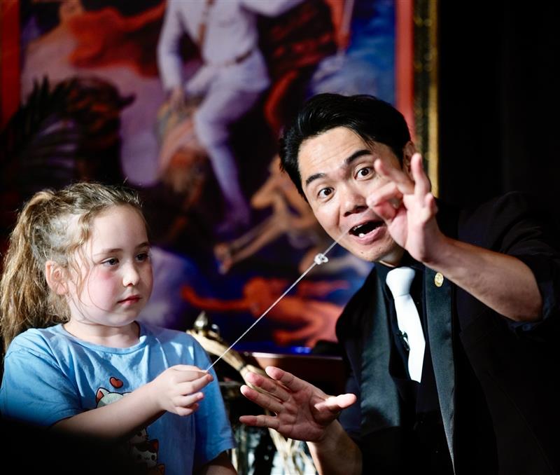Magician performing a trick with a young girl, showing her how to create a magical illusion with a string.