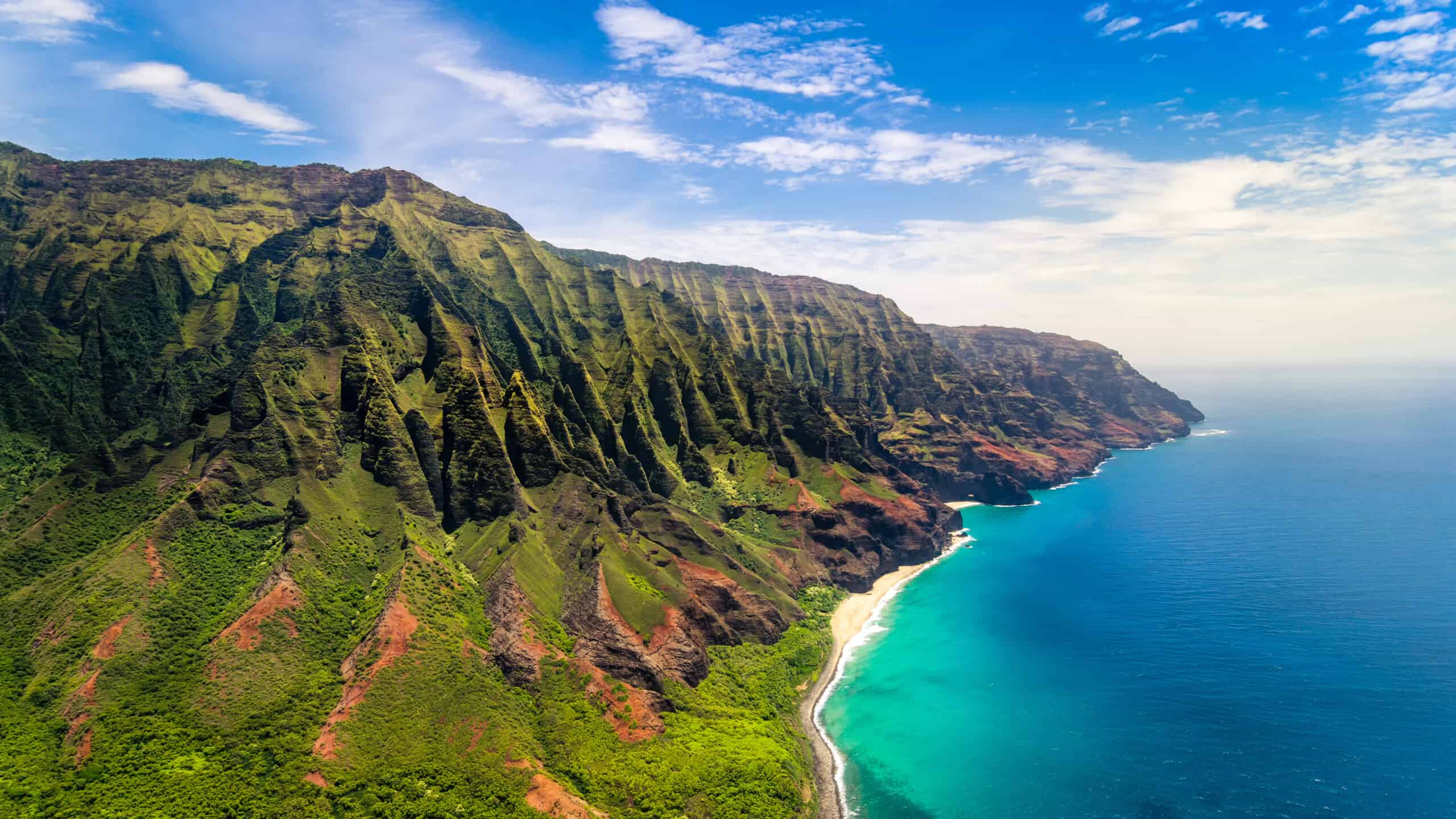 Aerial view of the Na Pali coastline in Hawaii, showcasing lush green cliffs and clear blue ocean waters.