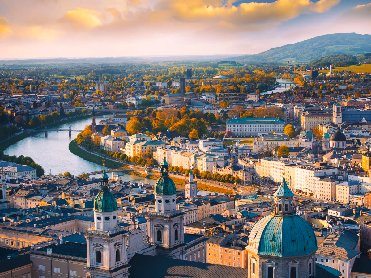 Panoramic view of Salzburg, Austria, showcasing the cityscape with historic buildings, bridges, and surrounding nature during sunset.